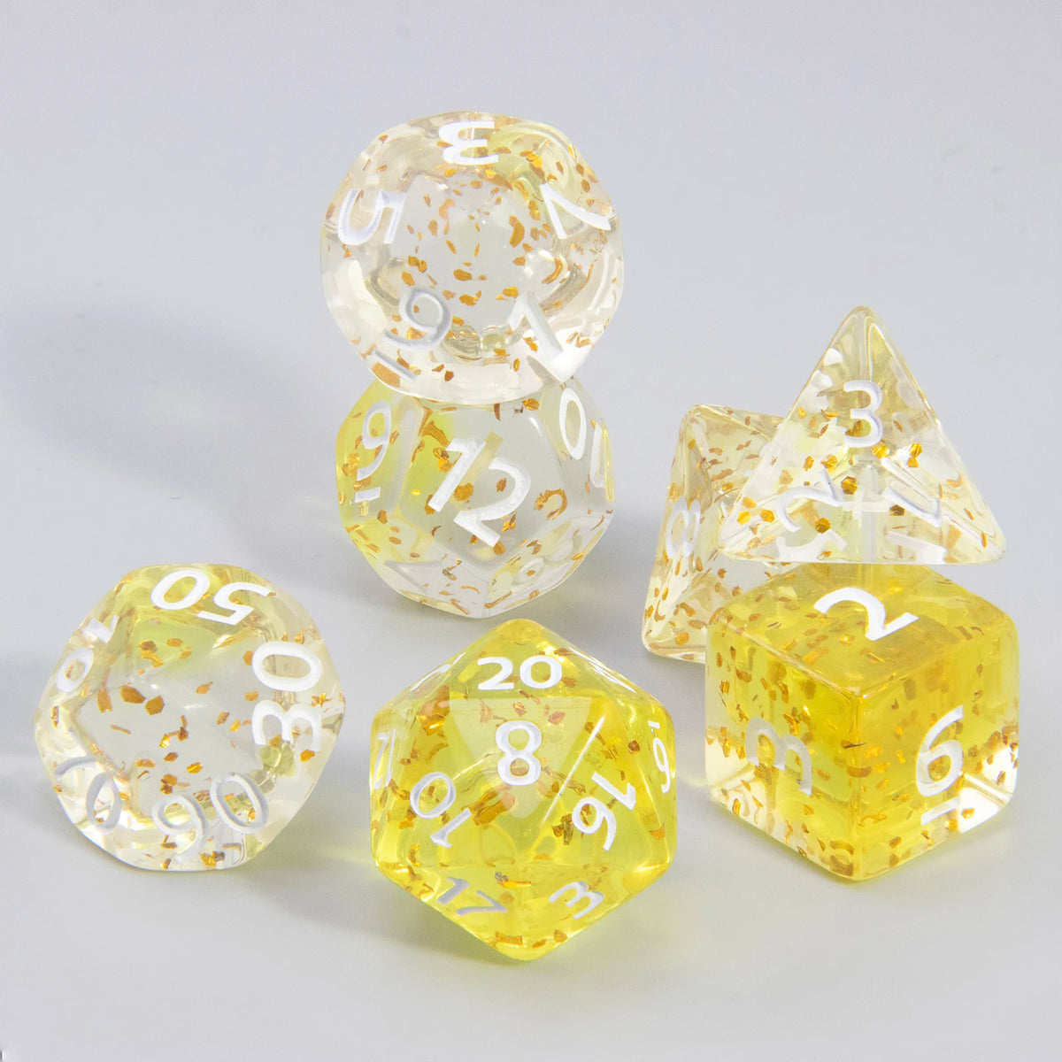A set of clear, glitter polyhedral dice including D4, D6, D8, D10, D12, D20, and D00 dice scattered on a white surface.