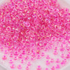 A pile of small, translucent pink and magenta glass rice beads for DIY jewelry and crafting.