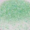 A close-up view of small, translucent green glass rice beads scattered in a clear container.