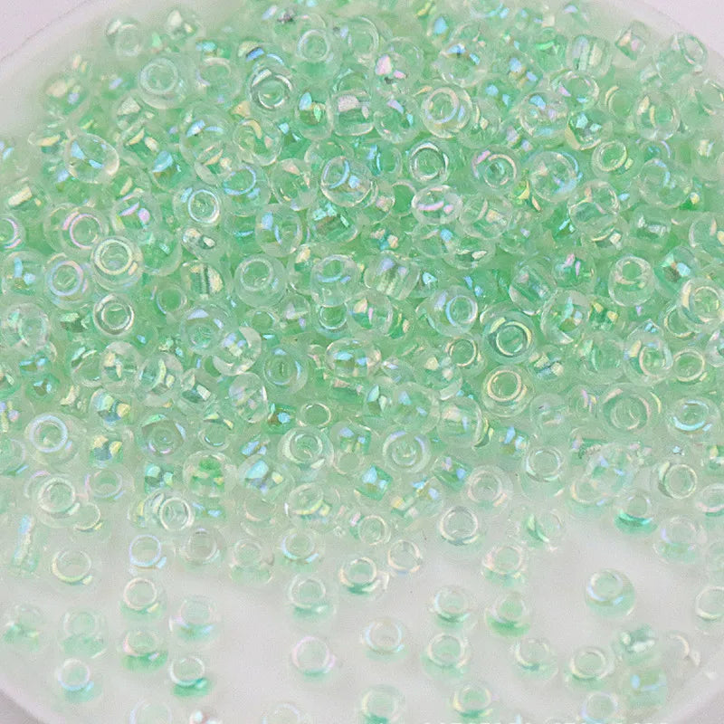 A close-up view of small, translucent green glass rice beads scattered in a clear container.