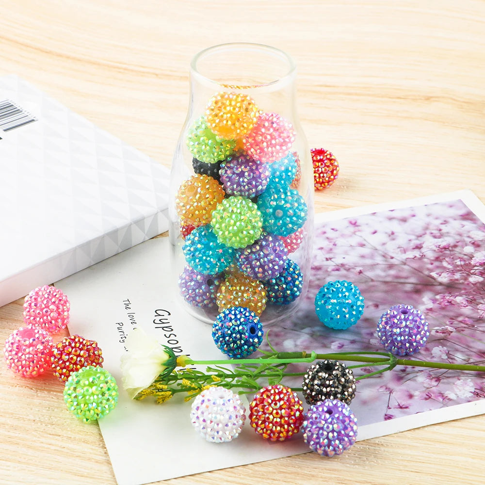 A clear glass jar filled with colorful rhinestone resin ball beads for jewelry making displayed on a wooden surface.