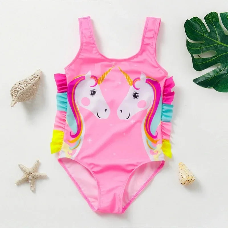 Pink kids mermaid unicorn one-piece swimsuit with rainbow trim lying on a white surface.