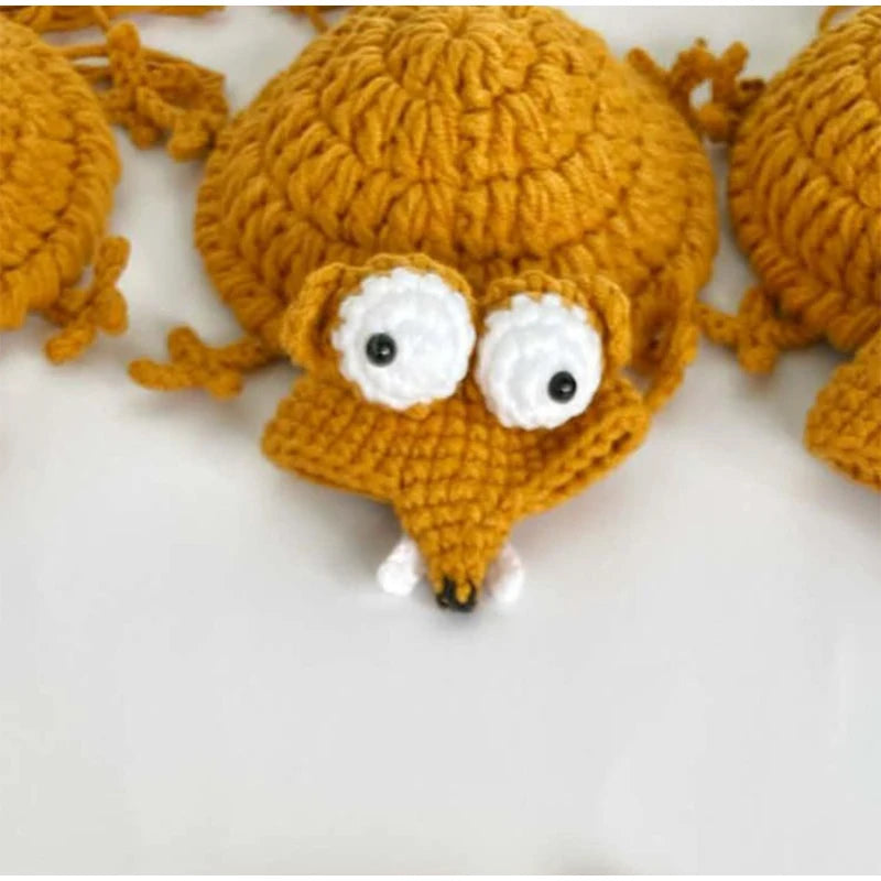 A handmade crochet lizard coaster in orange with white eyes and a textured body.