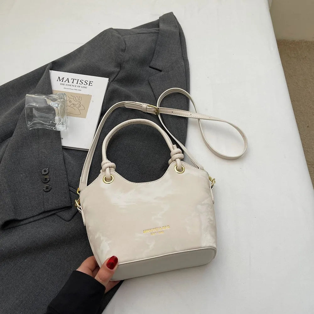 A cream canvas tote bag with gold hardware is shown next to a gray blazer and a piece of paper.