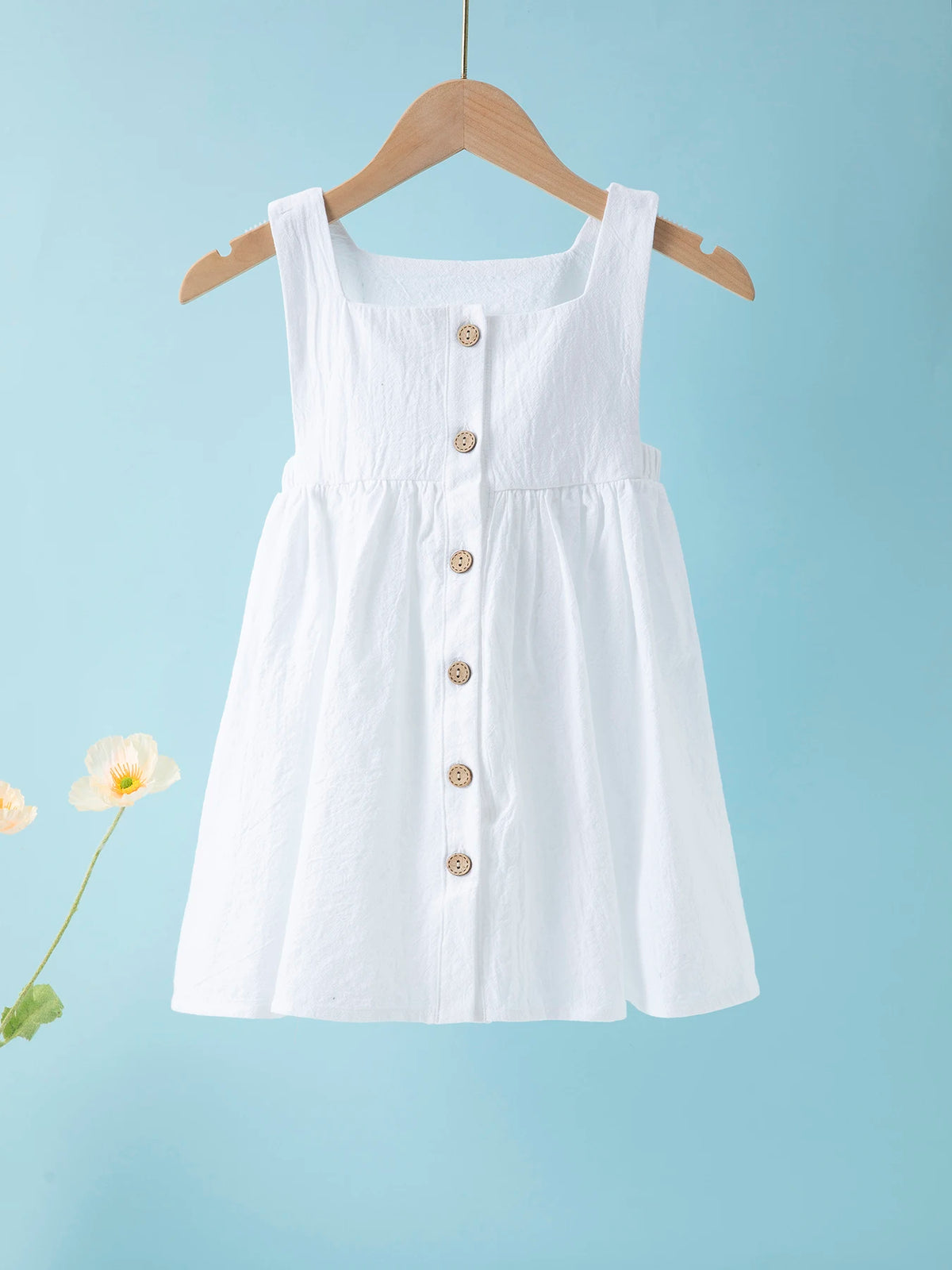 White summer cotton linen jumper dress for toddler girls hanging on a wooden hanger against a light blue background