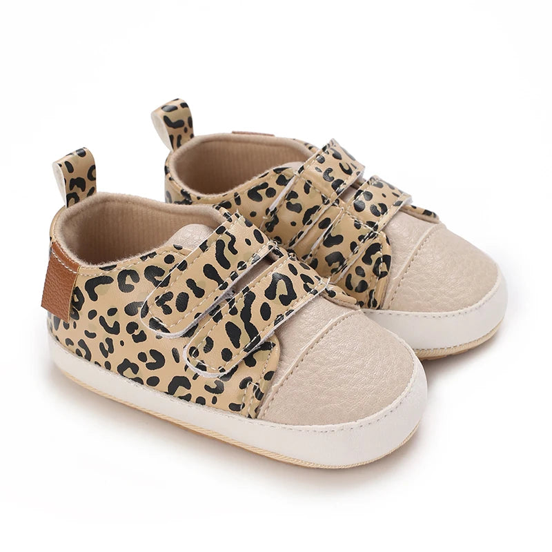 A pair of leopard print soft sole baby sneakers with tan fabric and brown accents.