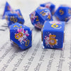 A set of blue resin dice showing numbers 0 through 6 with black kitten designs on a white background.