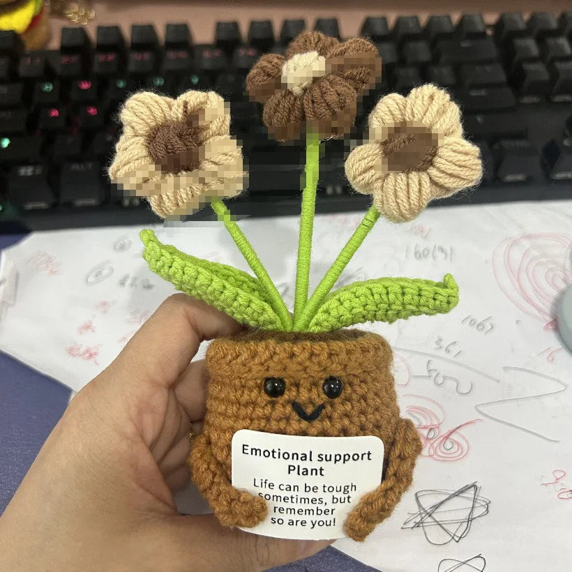 Handmade crochet sunflower plant with a brown pot and green leaves resting on paper.