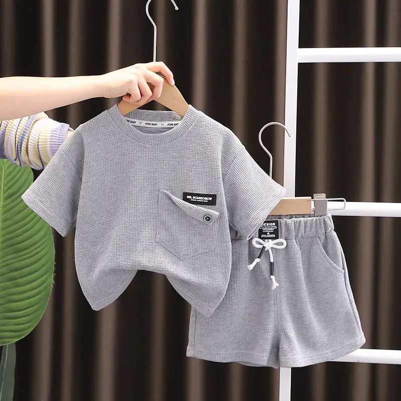A gray boys' summer cotton t-shirt and shorts set displayed on a hanger against a dark background.