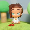 A blind box figure of a female character with brown hair and green eyes sitting on a green surface.