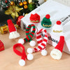 A set of mini knit Christmas hats and scarves in red, green, and white yarn displayed on a wooden surface.