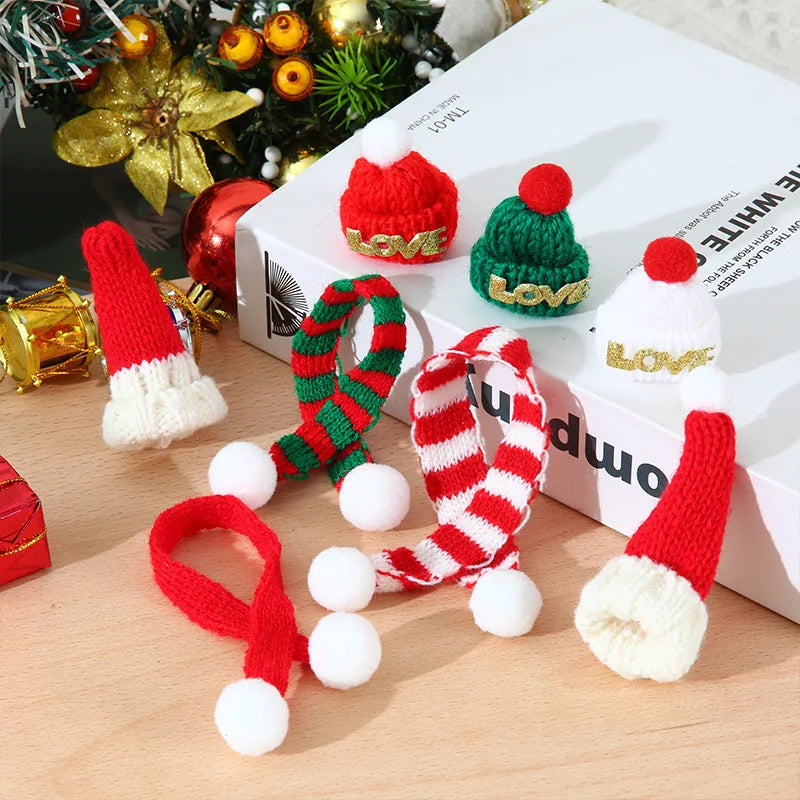 A set of mini knit Christmas hats and scarves in red, green, and white yarn displayed on a wooden surface.