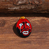 A red enamel lapel pin depicting a stylized, screaming face with wide blue eyes and open mouth against a black background.
