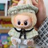 A handmade doll wearing a green grid cape and beret set, held by a person's hand.