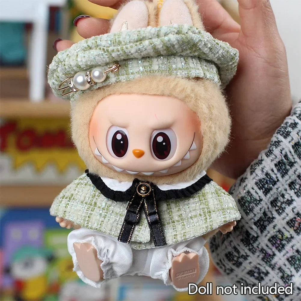 A handmade doll wearing a green grid cape and beret set, held by a person's hand.