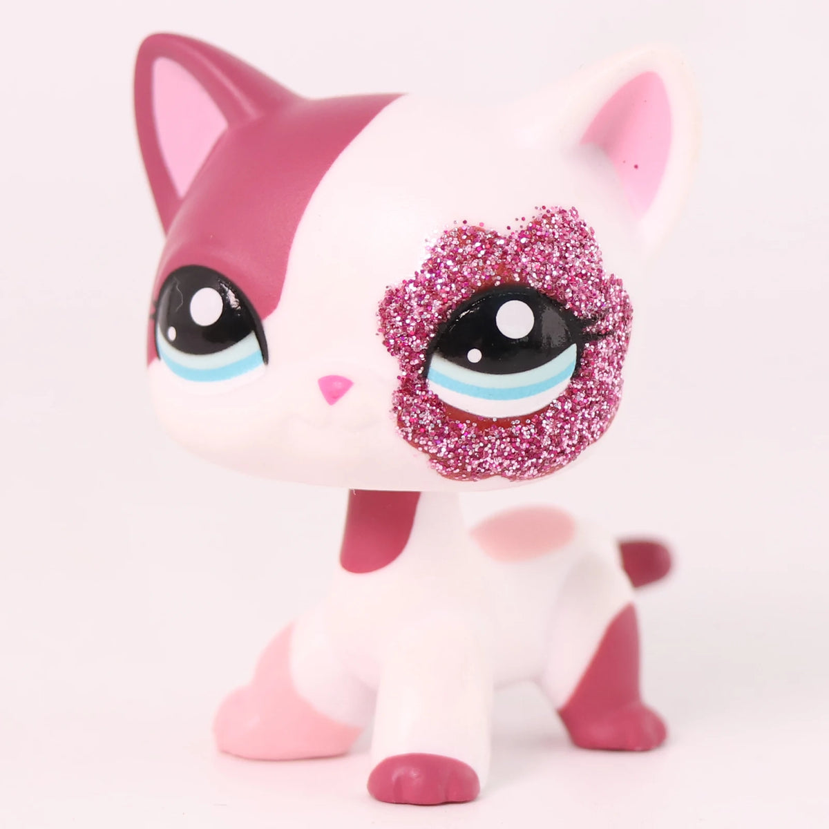 A pink and white shorthair cat bobble head figurine with sparkly purple eyes and pink accents.