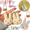 A fluffy white Miffy cartoon rabbit keychain pendant is shown being held in a hand against a striped fabric background.