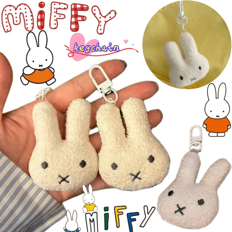 A fluffy white Miffy cartoon rabbit keychain pendant is shown being held in a hand against a striped fabric background.