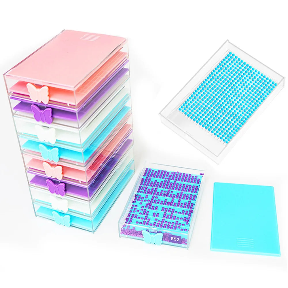 A stack of clear acrylic diamond painting storage trays with pink and purple colored beads and a separate blue tray.