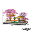 A miniature diorama featuring a pink sakura tree, a yellow house, and a train on a black base.