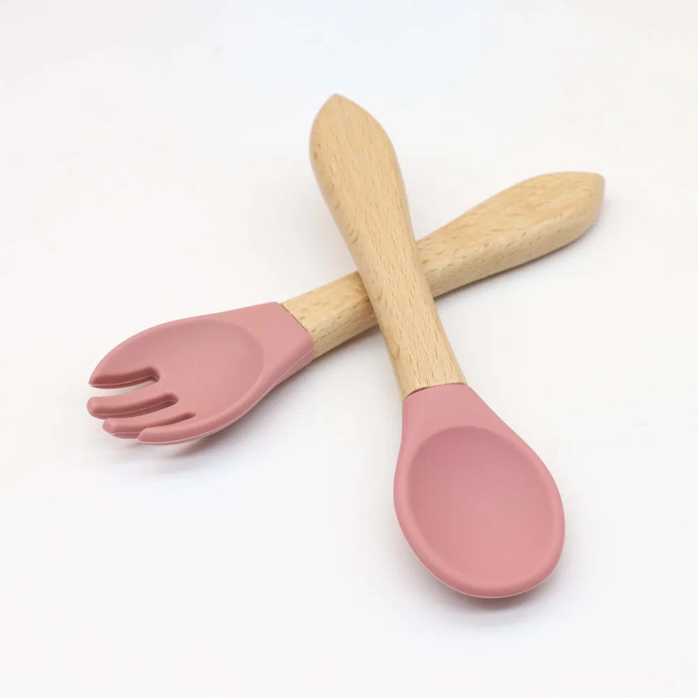 A wooden spoon and fork set with pink silicone plates and bowl