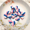 A collection of ten polymer clay marshmallow charms in blue and pink stripes arranged on a white plate.