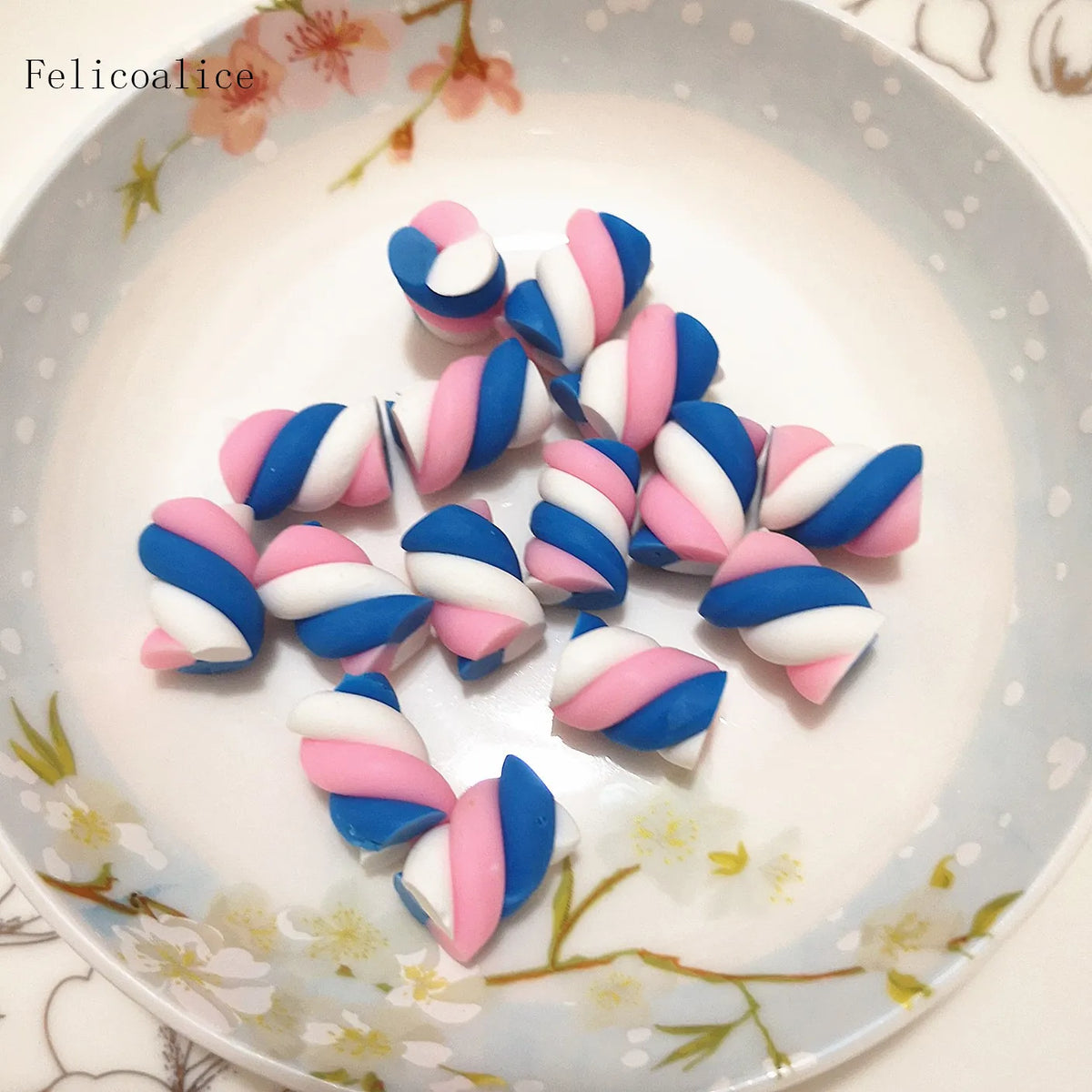 A collection of ten polymer clay marshmallow charms in blue and pink stripes arranged on a white plate.