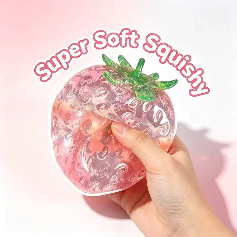 A hand holds a pink strawberry squishy stress ball with green leaves, demonstrating its soft texture.