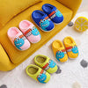 A collection of colorful dinosaur cartoon plush slippers in blue, pink, and yellow resting on a yellow fabric surface.