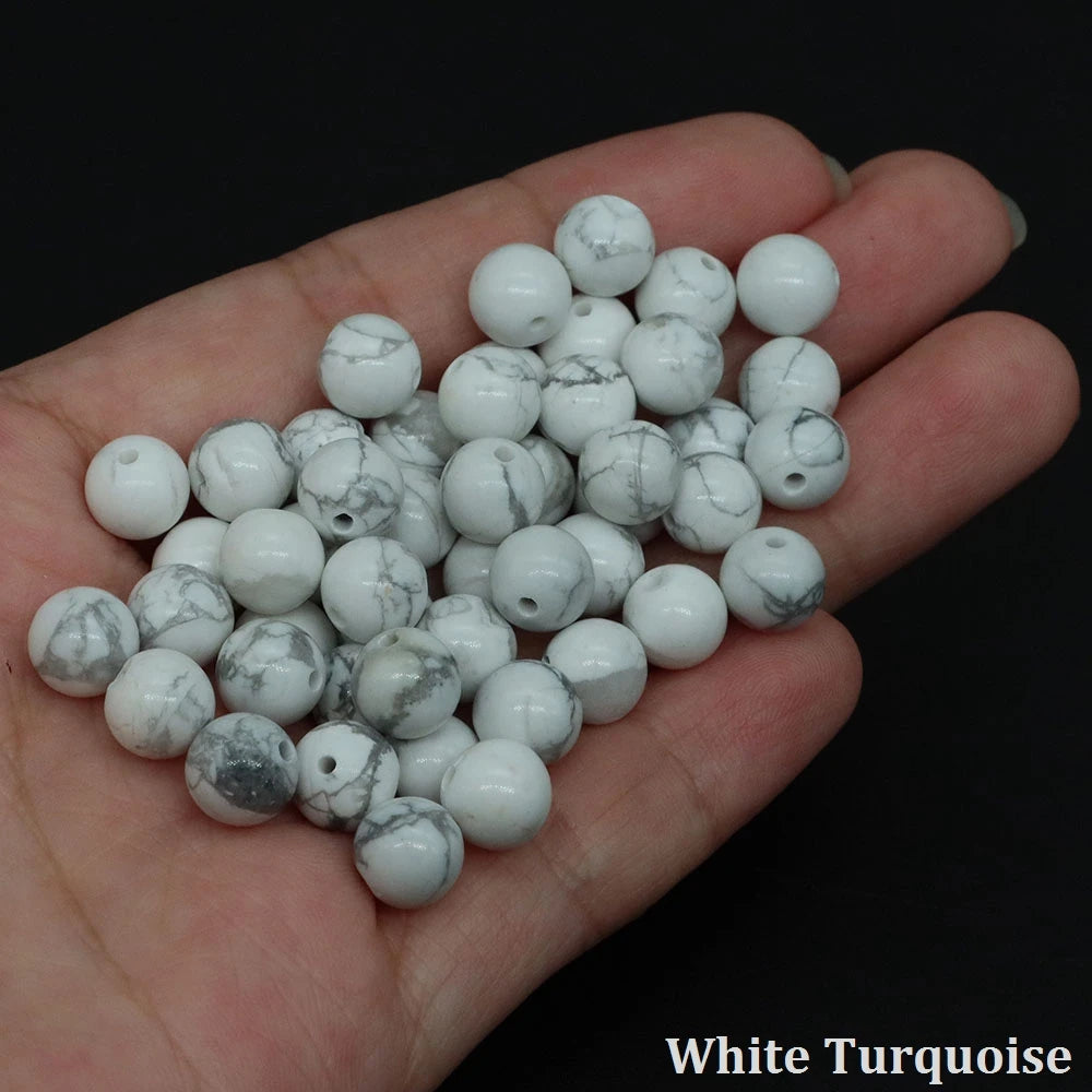A handful of white turquoise round beads for jewelry making resting on a hand.