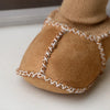 A close-up of cozy suede baby booties with a plush fur lining and white stitching detail.