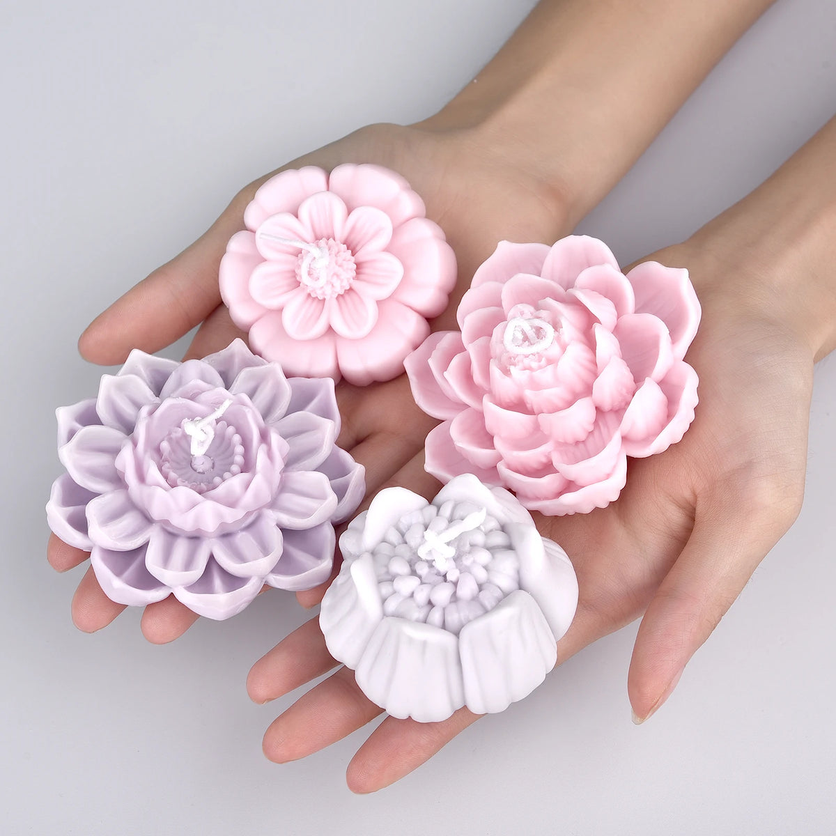 A hand holds a pink flower-shaped candle wax pigment set with various shades of pink and purple.