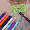 A collection of precision diamond painting pens and replacement tips arranged on a patterned surface with a green tray.