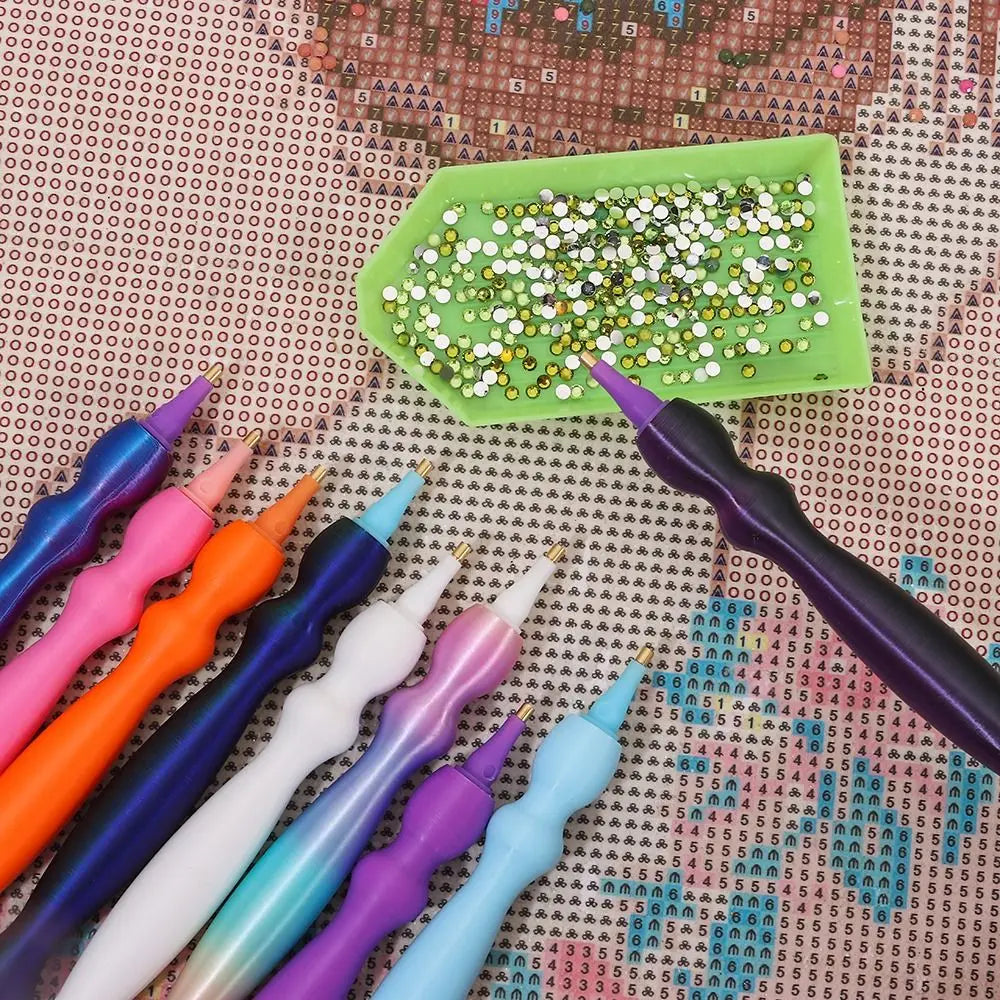 A collection of precision diamond painting pens and replacement tips arranged on a patterned surface with a green tray.