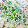 A pile of mixed resin rhinestone pearls in various shades of green and clear, iridescent colors for crafts and nail art.