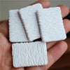 A hand holds four rectangular white miniature food items, likely a dollhouse set for beef steak and pasta.