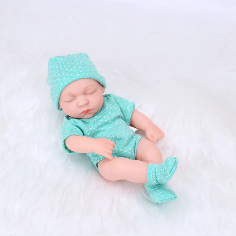 A realistic soft vinyl baby doll wearing a mint green polka dot outfit and matching hat, lying on a white surface.