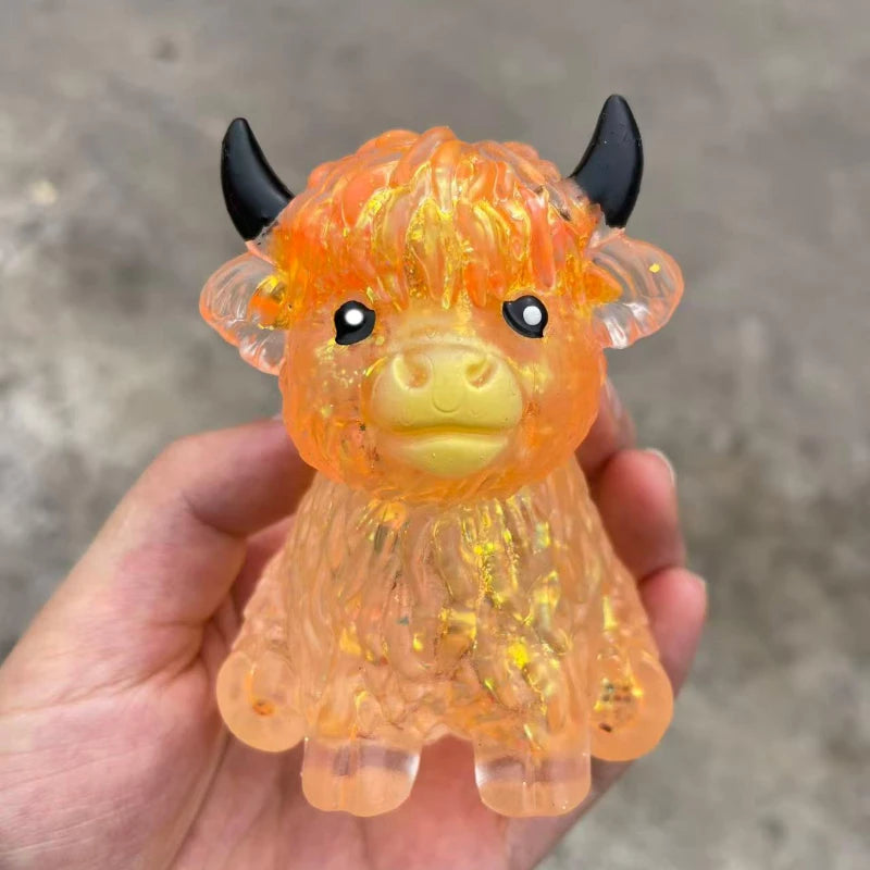 An orange glitter Highland cow squishy stress relief fidget toy is held in a hand.