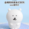 A white silicone bear lamp with black features sitting on a blue checkered cloth.