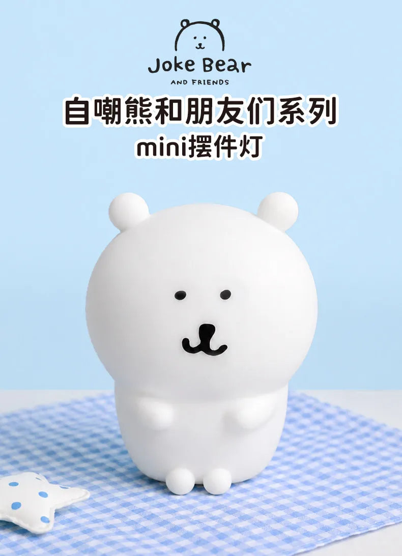 A white silicone bear lamp with black features sitting on a blue checkered cloth.