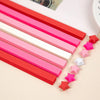 A collection of red, pink, and white origami star strips laid out diagonally on a light surface.