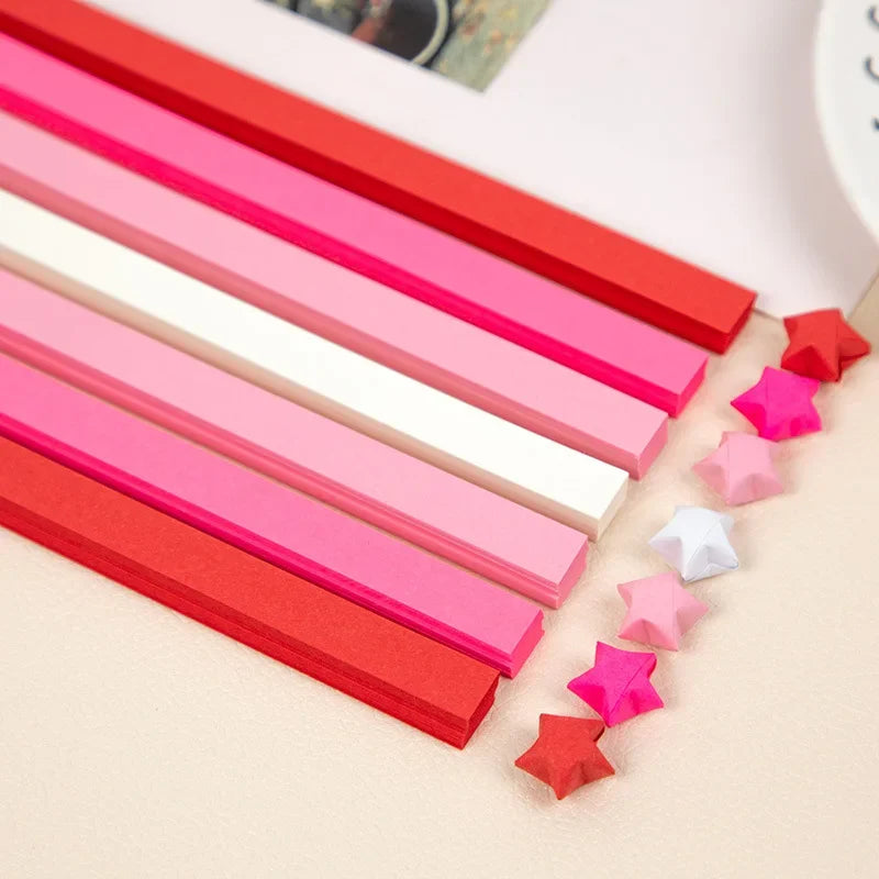 A collection of red, pink, and white origami star strips laid out diagonally on a light surface.