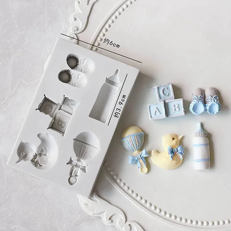 A white silicone cake molds set featuring various baby-themed shapes including a stroller, bottle, pacifier, and various smal