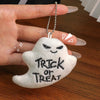 A white ghost-shaped plush keychain with black text reading Trick or Treat is held by a hand.