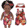 A realistic 12-inch African American baby doll wearing a floral patterned outfit with a bow in her hair.