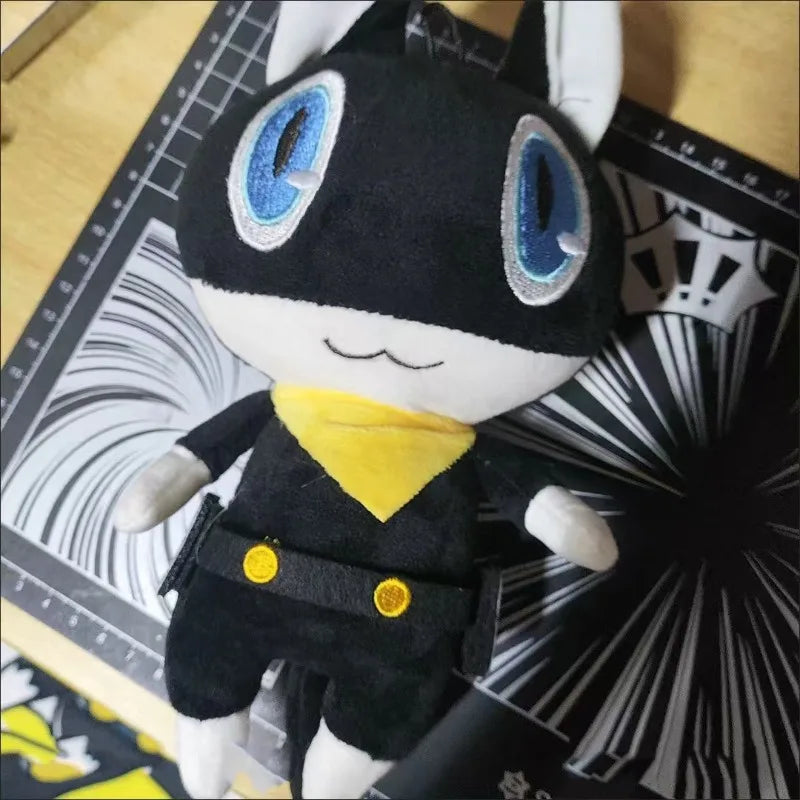 A black and yellow Persona 5 Morgana plush doll with blue eyes sitting on a black and white patterned surface.