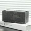 A dark camouflage miniature industrial iron storage box with an openable lid resting on a white book.