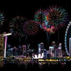 A night scene featuring fireworks over a city skyline with a large Ferris wheel reflected on the water.