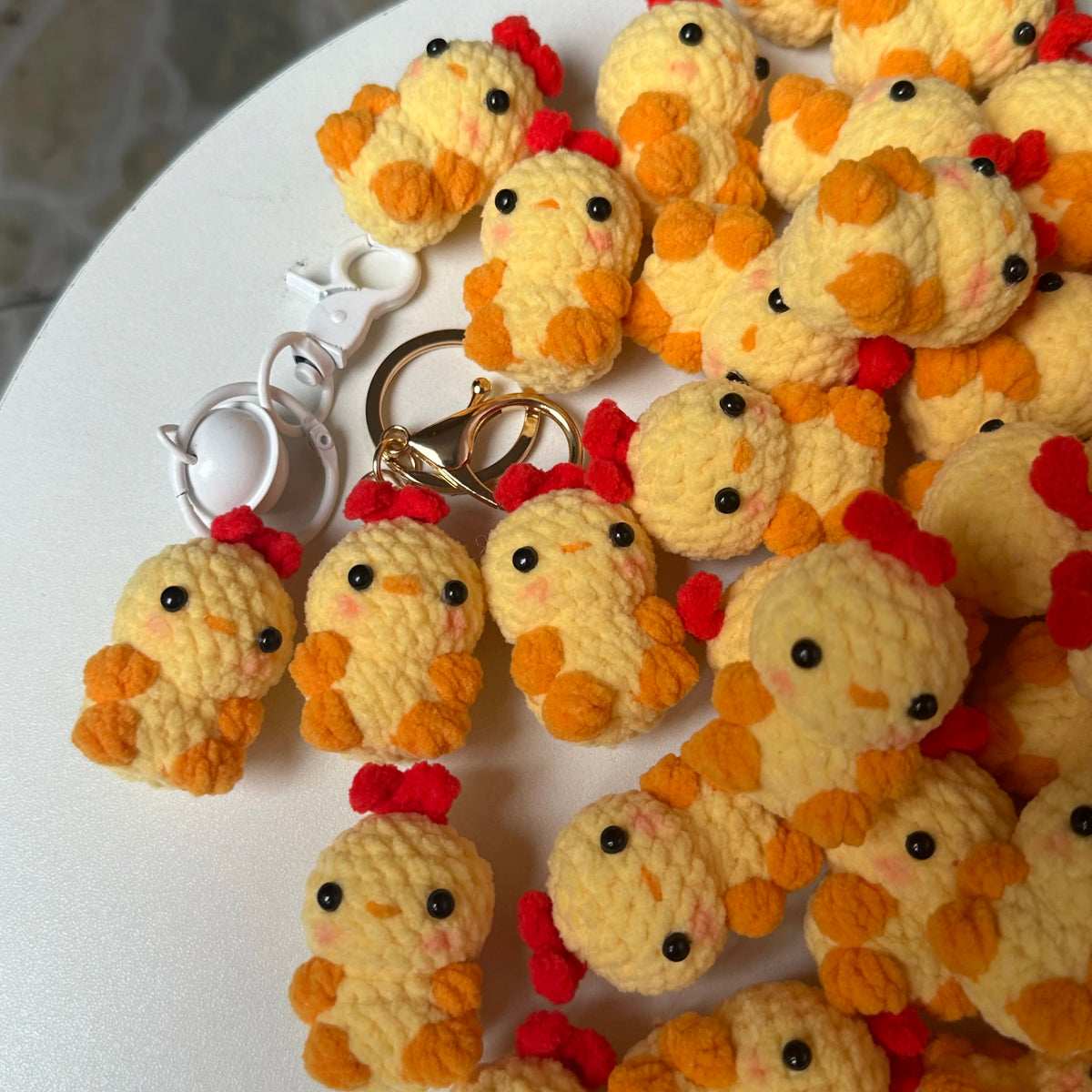 A collection of handmade crochet yellow and orange chick keychains arranged on a white surface.