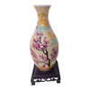 A ceramic flower vase with a pale yellow body decorated with pink and purple blossoms and blue accents, displayed on a dark s